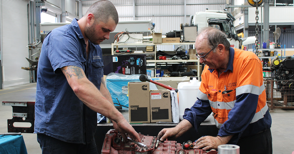Two mechanics working on a vehicle engineer in the middle of an workshop 