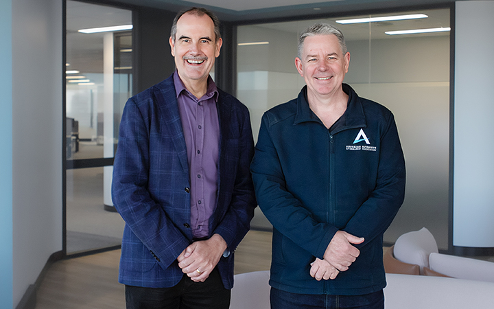 David and Stuart standing side by side smiling at the camera in an office environment