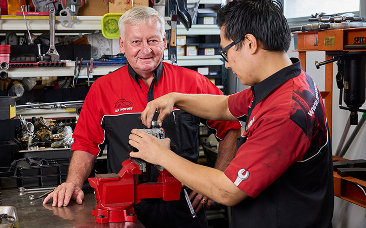 Two mechanics are actively working on a machine in a workshop, showcasing teamwork and technical skills.