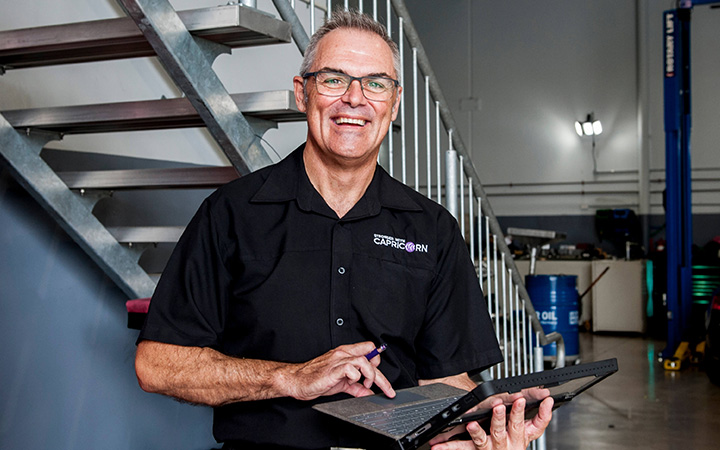 In a garage, a Capricorn Area Manager in a black shirt is engaged with a laptop