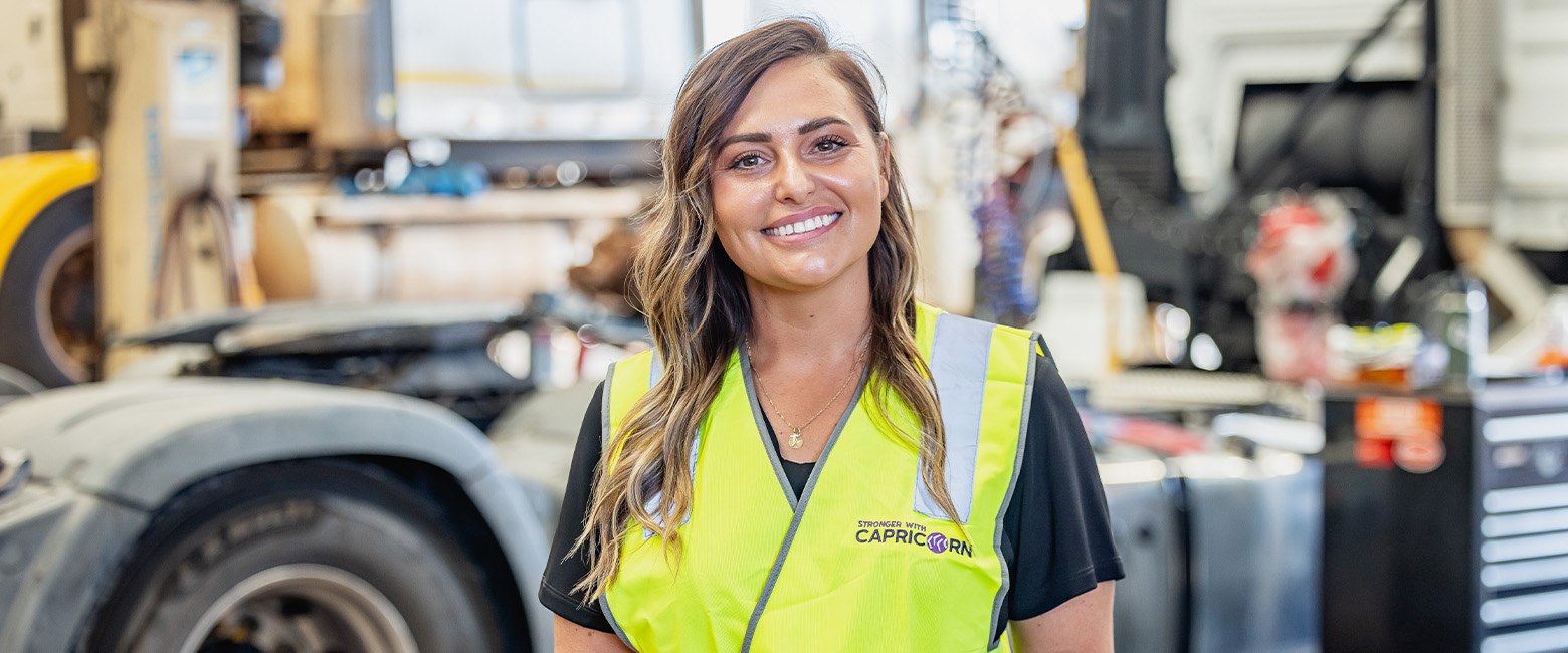 A woman wearing a yellow vest stands in front of a truck, representing the Capricorn team with pride and determination.