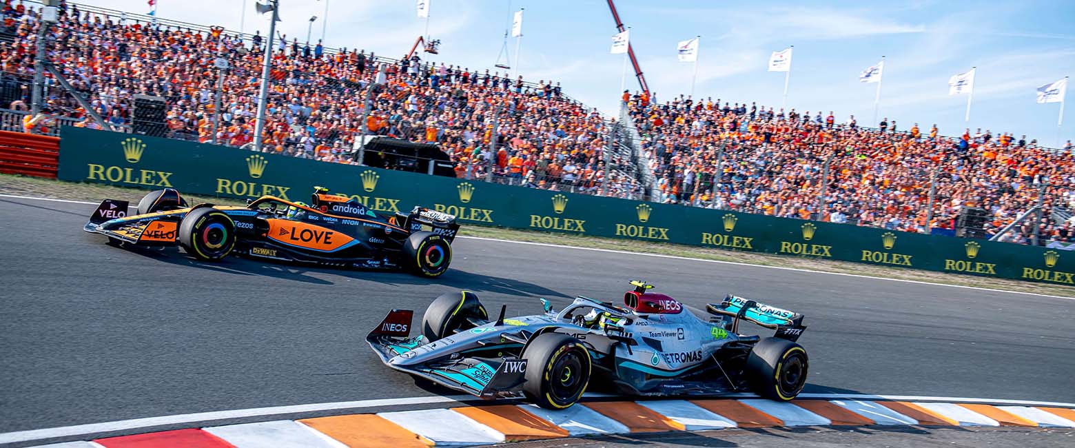 A thrilling scene of two F1 racing cars competing on the track, with a lively crowd cheering them on in the background.