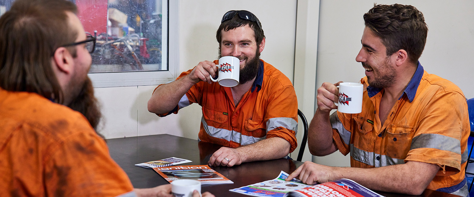 Three men in orange shirts enjoying coffee together at a table, engaged in conversation and laughter.